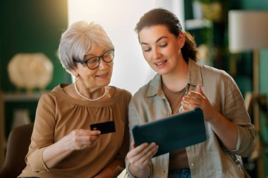 Genç ve yaşlı kadınlar online alışveriş için bilgisayar kullanıyorlar. Kızı evde annesine yardım ediyor..