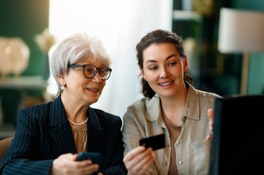 Genç ve yaşlı kadınlar online alışveriş için bilgisayar kullanıyorlar. Kızı evde annesine yardım ediyor..