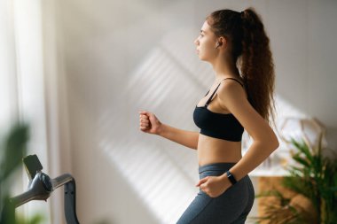 Ev antrenmanı. Koşu bandında koşan genç bir kadın..