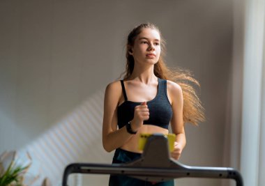 Ev antrenmanı. Koşu bandında koşan genç bir kadın..