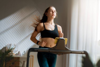 Ev antrenmanı. Koşu bandında koşan genç bir kadın..