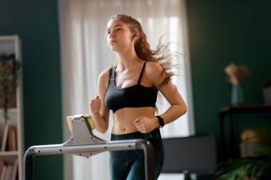 Ev antrenmanı. Koşu bandında koşan genç bir kadın..