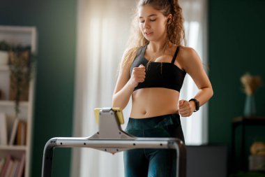 Ev antrenmanı. Koşu bandında koşan genç bir kadın..