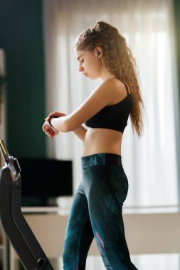 Ev antrenmanı. Koşu bandında koşan genç bir kadın..