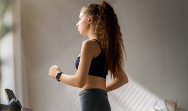 Ev antrenmanı. Koşu bandında koşan genç bir kadın..