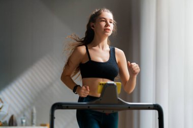 Ev antrenmanı. Koşu bandında koşan genç bir kadın..