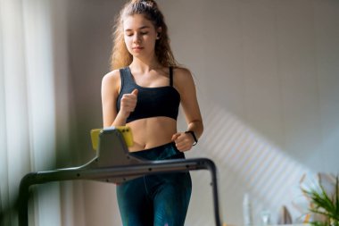 Ev antrenmanı. Koşu bandında koşan genç bir kadın..