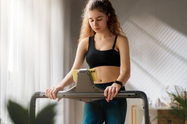 Ev antrenmanı. Koşu bandında koşan genç bir kadın..