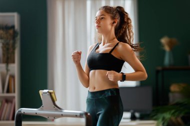 Ev antrenmanı. Koşu bandında koşan genç bir kadın..