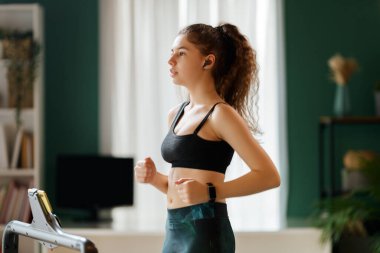 Ev antrenmanı. Koşu bandında koşan genç bir kadın..