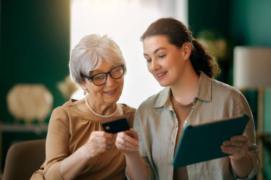 Genç ve yaşlı kadınlar online alışveriş için bilgisayar kullanıyorlar. Kızı evde annesine yardım ediyor..