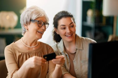 Genç ve yaşlı kadınlar online alışveriş için bilgisayar kullanıyorlar. Kızı evde annesine yardım ediyor..