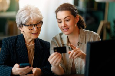 Genç ve yaşlı kadınlar online alışveriş için bilgisayar kullanıyorlar. Kızı evde annesine yardım ediyor..