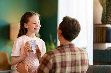 Çocuk kızı babasını tebrik ediyor ve ona bir hediye veriyor. Baba ve kız gülümsüyor. Aile tatili ve birliktelik.