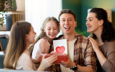 Çocuklar babalarını tebrik ediyor ve ona kartpostal ve hediye veriyorlar. Baba, annem ve kızlar gülümsüyor ve sarılıyorlar. Aile tatili ve birliktelik.