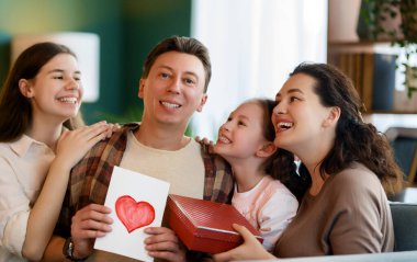 Çocuklar babalarını tebrik ediyor ve ona kartpostal ve hediye veriyorlar. Baba, annem ve kızlar gülümsüyor ve sarılıyorlar. Aile tatili ve birliktelik.