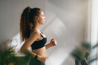 Ev antrenmanı. Koşu bandında koşan genç bir kadın..