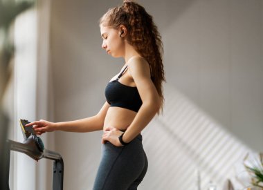 Ev antrenmanı. Koşu bandında koşan genç bir kadın..