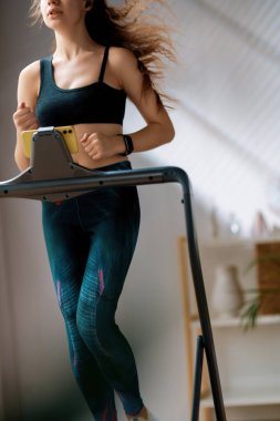 Ev antrenmanı. Koşu bandında koşan genç bir kadın..