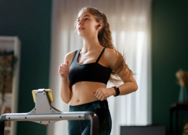 Ev antrenmanı. Koşu bandında koşan genç bir kadın..