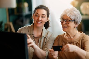 Genç ve yaşlı kadınlar online alışveriş için bilgisayar kullanıyorlar. Kızı evde annesine yardım ediyor..