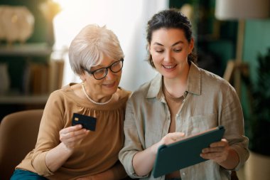 Genç ve yaşlı kadınlar online alışveriş için bilgisayar kullanıyorlar. Kızı evde annesine yardım ediyor..