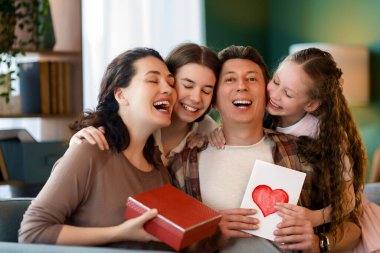 Çocuklar babalarını tebrik ediyor ve ona kartpostal ve hediye veriyorlar. Baba, annem ve kızlar gülümsüyor ve sarılıyorlar. Aile tatili ve birliktelik.