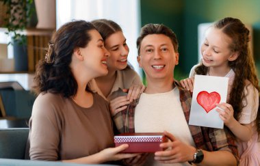 Çocuklar babalarını tebrik ediyor ve ona kartpostal ve hediye veriyorlar. Baba, annem ve kızlar gülümsüyor ve sarılıyorlar. Aile tatili ve birliktelik.