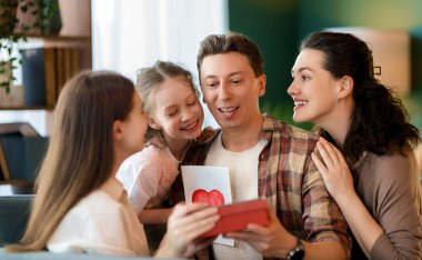Çocuklar babalarını tebrik ediyor ve ona kartpostal ve hediye veriyorlar. Baba, annem ve kızlar gülümsüyor ve sarılıyorlar. Aile tatili ve birliktelik.