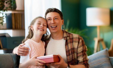 Çocuk kızı babasını tebrik ediyor ve ona bir hediye veriyor. Baba ve kız gülümsüyor. Aile tatili ve birliktelik.