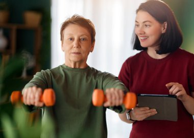 Kıdemli kadın halter egzersizi yapıyor. Evde fizik tedaviye yardım eden bir hemşire.