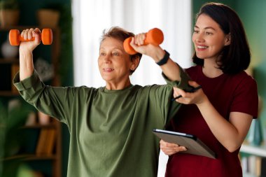 Kıdemli kadın halter egzersizi yapıyor. Evde fizik tedaviye yardım eden bir hemşire.