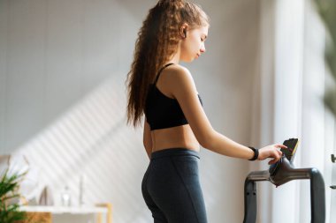 Ev antrenmanı. Koşu bandında koşan genç bir kadın..