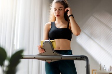 Ev antrenmanı. Koşu bandında koşan genç bir kadın..