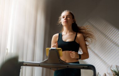 Ev antrenmanı. Koşu bandında koşan genç bir kadın..