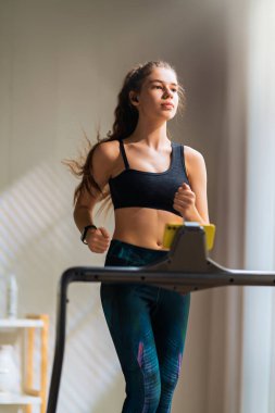 Ev antrenmanı. Koşu bandında koşan genç bir kadın..