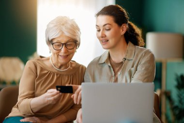 Genç ve yaşlı kadınlar online alışveriş için bilgisayar kullanıyorlar. Kızı evde annesine yardım ediyor..