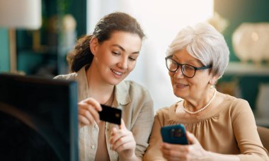 Genç ve yaşlı kadınlar online alışveriş için bilgisayar kullanıyorlar. Kızı evde annesine yardım ediyor..