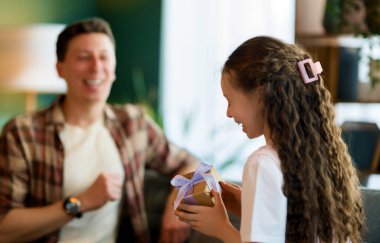 Çocuk kızı babasını tebrik ediyor ve ona bir hediye veriyor. Baba ve kız gülümsüyor. Aile tatili ve birliktelik.