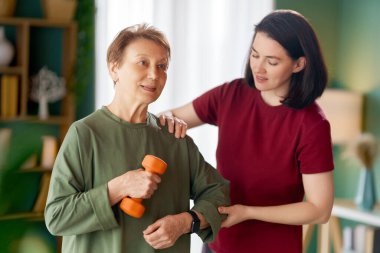 Kıdemli kadın halter egzersizi yapıyor. Evde fizik tedaviye yardım eden bir hemşire.