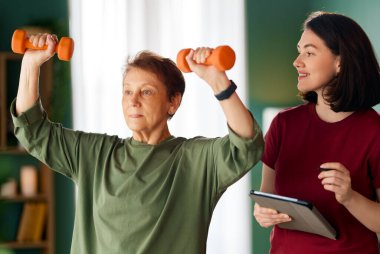 Kıdemli kadın halter egzersizi yapıyor. Evde fizik tedaviye yardım eden bir hemşire.