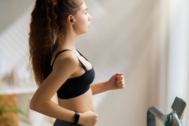 Ev antrenmanı. Koşu bandında koşan genç bir kadın..