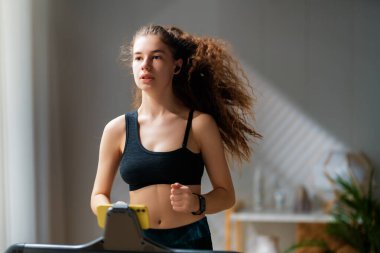 Ev antrenmanı. Koşu bandında koşan genç bir kadın..