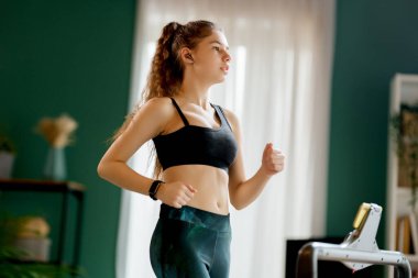 Ev antrenmanı. Koşu bandında koşan genç bir kadın..