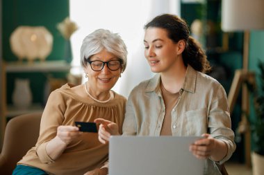 Genç ve yaşlı kadınlar online alışveriş için bilgisayar kullanıyorlar. Kızı evde annesine yardım ediyor..