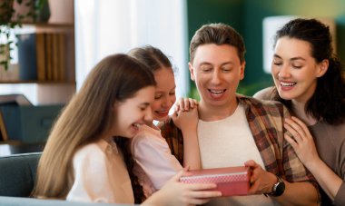 Çocuklar babalarını kutluyor ve ona hediye veriyorlar. Baba, annem ve kızlar gülümsüyor ve sarılıyorlar. Aile tatili ve birliktelik.