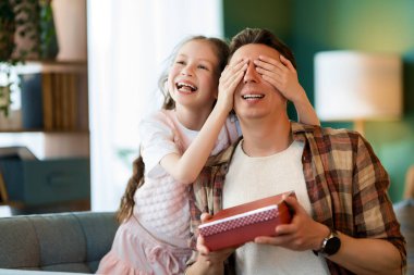 Çocuk kızı babasını tebrik ediyor ve ona bir hediye veriyor. Baba ve kız gülümsüyor. Aile tatili ve birliktelik.