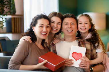 Çocuklar babalarını tebrik ediyor ve ona kartpostal ve hediye veriyorlar. Baba, annem ve kızlar gülümsüyor ve sarılıyorlar. Aile tatili ve birliktelik.