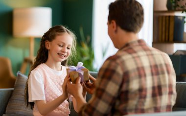 Çocuk kızı babasını tebrik ediyor ve ona bir hediye veriyor. Baba ve kız gülümsüyor. Aile tatili ve birliktelik.