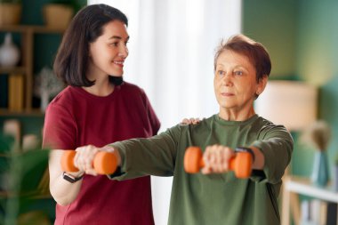 Kıdemli kadın halter egzersizi yapıyor. Evde fizik tedaviye yardım eden bir hemşire.